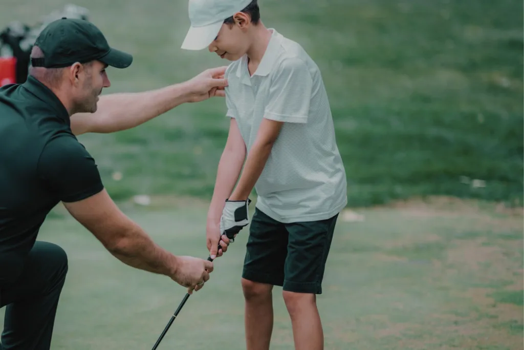 A golf instructor coaching a little golfer.
